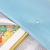 A close-up view of a light blue fabric with a cut-out star, partially covering a book with a floral pattern and text. Produktbild-Vorschau