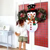 A young girl is touching a large felt snowman decoration hanging on a door with a red plaid background. Náhľad obrázku produktu