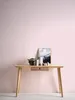 A wooden desk against a pink wall with decorative items on top. Produktbild-Vorschau