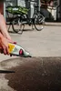 A person is pouring a cleaning product from a bottle onto the ground next to a bicycle. Produktbild-Vorschau