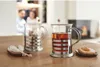 Two tea glasses with tea and rock candy on a wooden table, with people in the background. Produktbild-Vorschau
