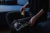 A person is sitting on a couch, holding a small flashlight and keys, and looking into a bag. Anteprima dell’immagine prodotto