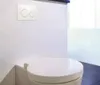 A close-up view of a modern toilet with a flush plate mounted on the wall above it. Náhľad obrázku produktu