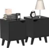 Two black nightstands are shown against a white background. The nightstand on the left has books and a candle on top. The nightstand on the right has a lamp and an alarm clock on top. Podgląd zdjęcia produktu