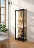 A glass display cabinet filled with bottles and decorative items, placed in a room with a large window and a chair. Produktbild-Vorschau