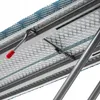 A close-up view of the underside of a metal structure, possibly a folding table or ironing board, showing a red-handled latch mechanism and a mesh metal surface. Náhled obrázku produktu