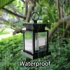 A solar lantern with a candle inside is hanging from a tree branch in the rain. Voir les images du produit