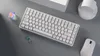 A white mechanical keyboard and a white mouse are arranged on a gray surface, with two small decorative cubes nearby. Anteprima dell’immagine prodotto