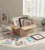 A cardboard box filled with picture frames and several picture frames and photos laid out on a wooden floor. Produktbild-Vorschau