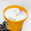 A close-up view of a yellow spreader filled with white granular material, likely salt or fertilizer, on a white background. Produktbild-Vorschau