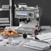 An espresso machine is set up on a counter with bread, coffee beans, a glass of water, a newspaper, and a keyboard. Produktbild-Vorschau