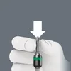A hand wearing a white glove holds a screwdriver bit with a ratchet function. A white arrow points downwards towards the bit. Anteprima dell’immagine prodotto