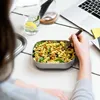 A person is eating pasta from a lunchbox at a desk with a laptop and a glass of water. Podgląd zdjęcia produktu
