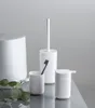 A set of white bathroom accessories including a trash can, toilet brush holder, toothbrush holder, and soap dispenser, arranged on a reflective surface with a plain gray background. Náhled obrázku produktu