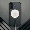 A black iPhone case with a white MagSafe charger attached, placed on a gray textured surface with dark diagonal elements. Anteprima dell’immagine prodotto