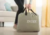 A person is holding a large khaki bag with the Intex logo on it, in a living room setting. Produktbild-Vorschau