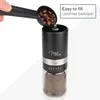 A hand is shown pouring coffee beans into a manual coffee grinder. The grinder has a glass bottom filled with ground coffee. Anteprima dell’immagine prodotto
