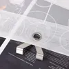 A close-up view of a white roller blind with circular patterns, showing a metal grommet and a metal clip. Text from a recipe book is visible underneath. Produktbild-Vorschau