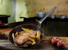 A rustic kitchen scene with a frying pan containing steak and potatoes on a wooden table, with tomatoes in the foreground. Náhled obrázku produktu