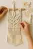 Hands are shown working on a macrame wall hanging with a leaf pattern, with dried flowers and seed pods arranged nearby. Produktbild-Vorschau