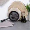A cast iron pan with oil and a bottle of olive oil are displayed on a surface with wooden discs and a plant in the background. Produktbild-Vorschau