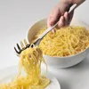 A hand is using a spaghetti server to lift pasta from a bowl onto a plate. Podgląd zdjęcia produktu