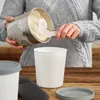 A person is pouring ice cream from a metal container into a white plastic container. Produktbild-Vorschau