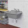 A grey sink with a silver faucet is mounted on a light grey tiled wall. Storage drawers are visible to the left. Produktbild-Vorschau