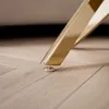 Close-up of a gold-colored furniture leg with a silver adjustable foot on a light-colored wooden floor. Produktbild-Vorschau