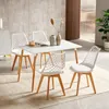 A dining set with a white table and four white chairs with wooden legs, placed on a rug in a modern room. Náhled obrázku produktu