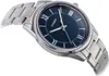 A close-up, angled shot of a men's wristwatch with a blue dial and a silver metal band, set against a white background. Podgląd zdjęcia produktu