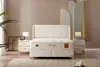 A bedroom scene featuring a white boxspring bed set with matching nightstands and lamps. Produktbild-Vorschau