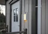 A solar-powered wall light mounted on the side of a wooden house next to a white door. Podgląd zdjęcia produktu