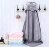 A hooded towel with an elephant design hangs on hooks, with stacks of folded towels in pink, white, and blue below. Produktbild-Vorschau