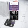 A person's legs are visible standing on a tiled floor next to a black digital scale. The scale displays various body metrics. Produktbild-Vorschau
