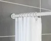 A close-up view of a white shower curtain rod with hooks and a white shower curtain hanging from it, mounted on a gray tiled wall. Produktbild-Vorschau