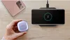 A hand holds a purple wireless charging case next to a rose gold smartphone and a black wireless charging pad with a phone charging on it. Produktbild-Vorschau