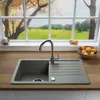 A kitchen sink with a faucet and a bowl of oranges, set against a window view of a green landscape. Produktbild-Vorschau