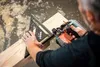 A carpenter is using a circular saw and a square to cut a piece of wood. Voir les images du produit