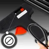 Close-up of a black hot glue gun with an orange trigger, showing a hand holding a black glue stick. A circular icon with a line through it is visible on the left. Voir les images du produit
