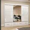 A white sliding door wardrobe with a mirrored section, set up in a bedroom with a bed and bedside table. Produktbild-Vorschau