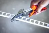 A hand is using a pair of orange-handled shears to cut a white plastic strip with square cutouts. Anteprima dell’immagine prodotto
