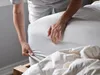 A person is tucking a fitted sheet onto a mattress. Produktbild-Vorschau