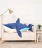 A large blue shark plush toy is placed on a sofa in a living room setting. Produktbild-Vorschau
