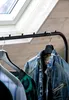 Close-up of clothing hanging on a rack in front of a skylight and textured wall. Náhľad obrázku produktu