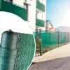 A roll of green privacy screen mesh is shown in the foreground, with a fence covered in the same mesh in the background, attached to a building with balconies. Produktbild-Vorschau