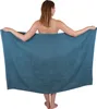 A woman is holding a large blue towel in front of her. Produktbild-Vorschau