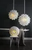 Three paper star lanterns are displayed, two hanging and one on a chair, with a draped cloth and a small plant on a table in the background. Podgląd zdjęcia produktu