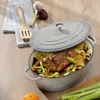 A cast iron pot with food inside, placed on a wooden surface with kitchen utensils and ingredients. Anteprima dell’immagine prodotto