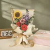 A 3D wooden puzzle bouquet is displayed on a table next to a perpetual calendar and a gift box. Produktbild-Vorschau